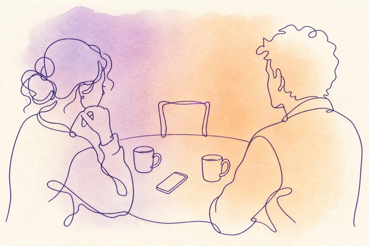 Two mugs of tea on a table with an empty chair on the far side and a phone face up between them
