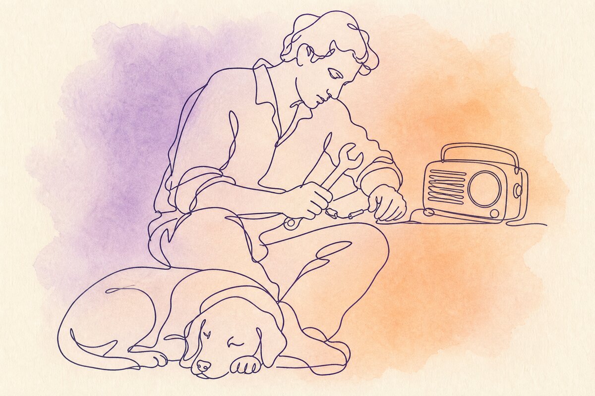 A man alone in a garage workshop, a radio on the bench and a dog asleep at his feet